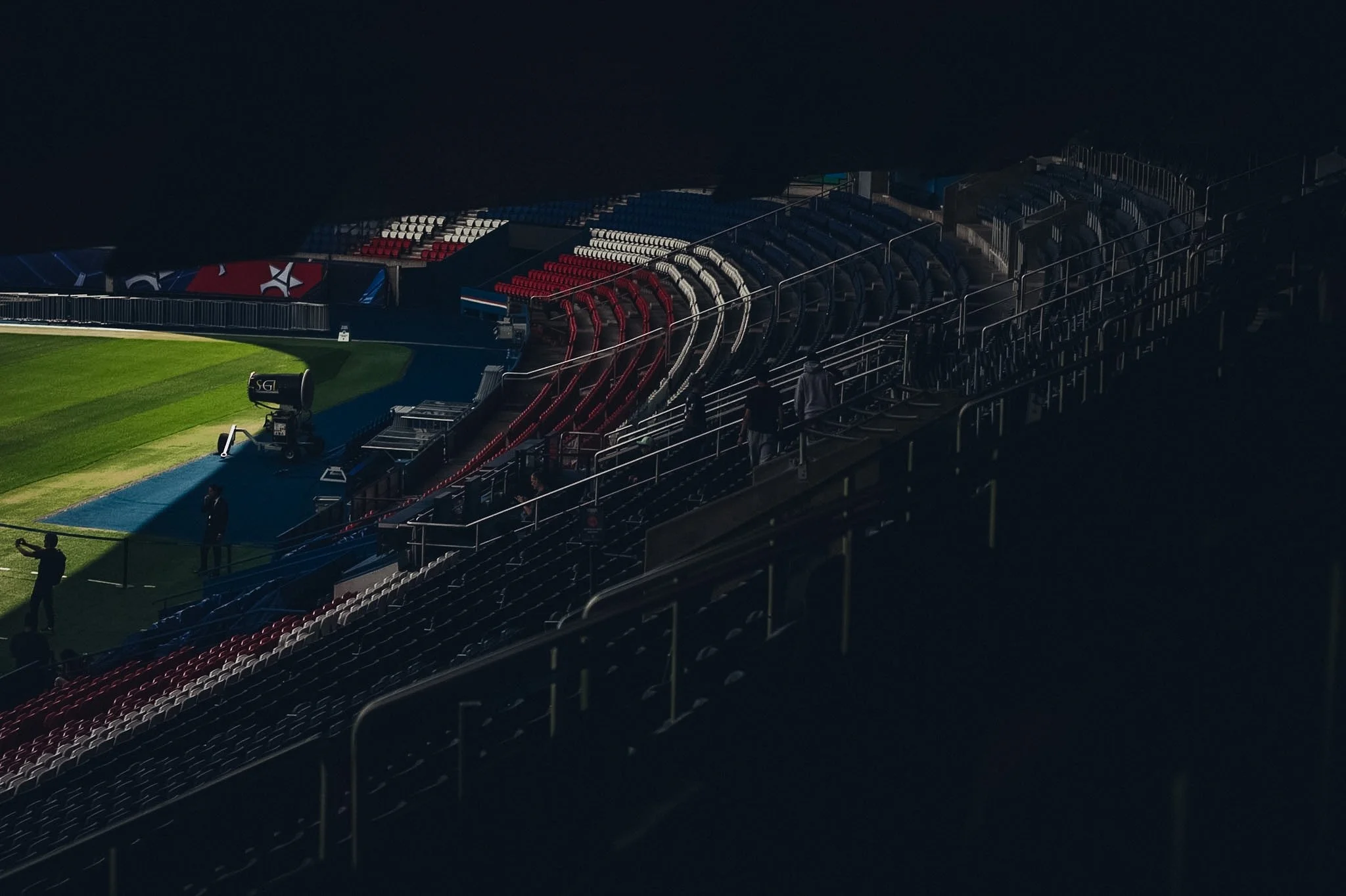 Empty stadium seats near a brightly lit sports field at night.