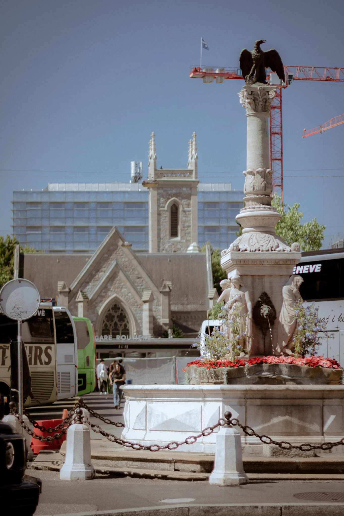 Statue of an eagle perched on a column in a city square with historic and modern buildings in the background, along with construction cranes.