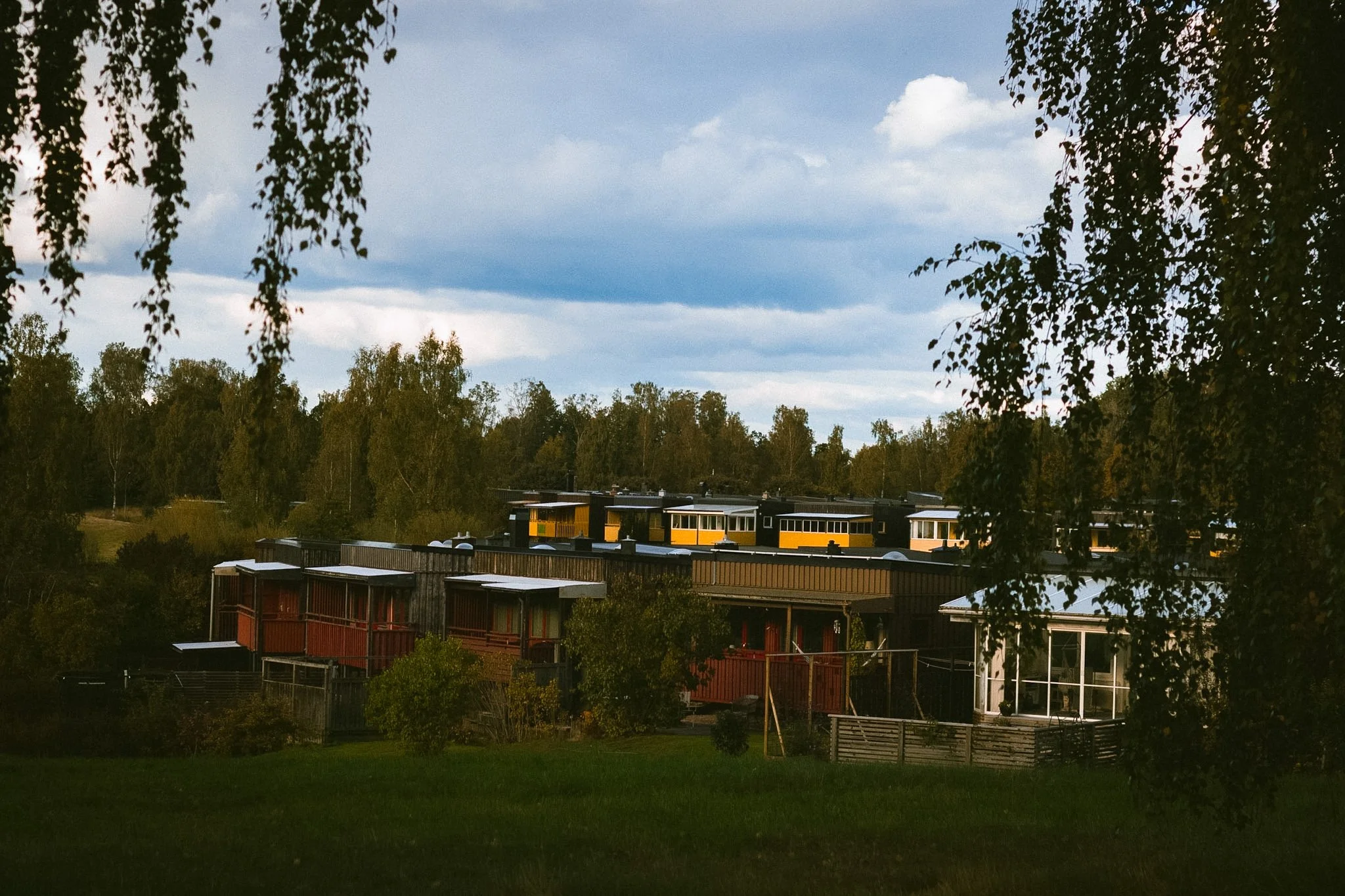 A view of trees and colorful houses in a neighborhood, with a sky filled with clouds overhead.