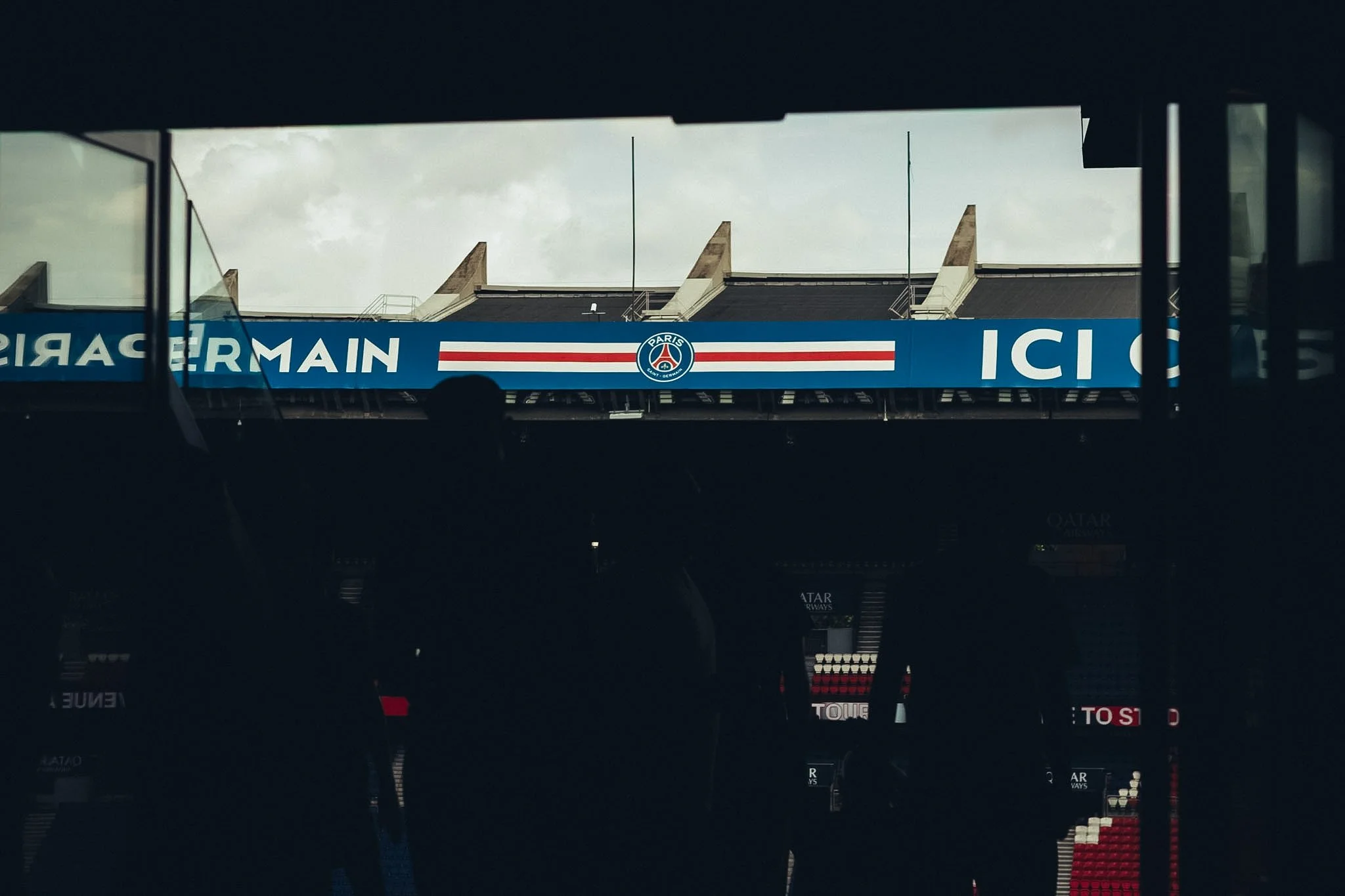 A view of a Paris Saint-Germain (PSG) advertisement sign seen from underneath a structure, with the sky in the background.