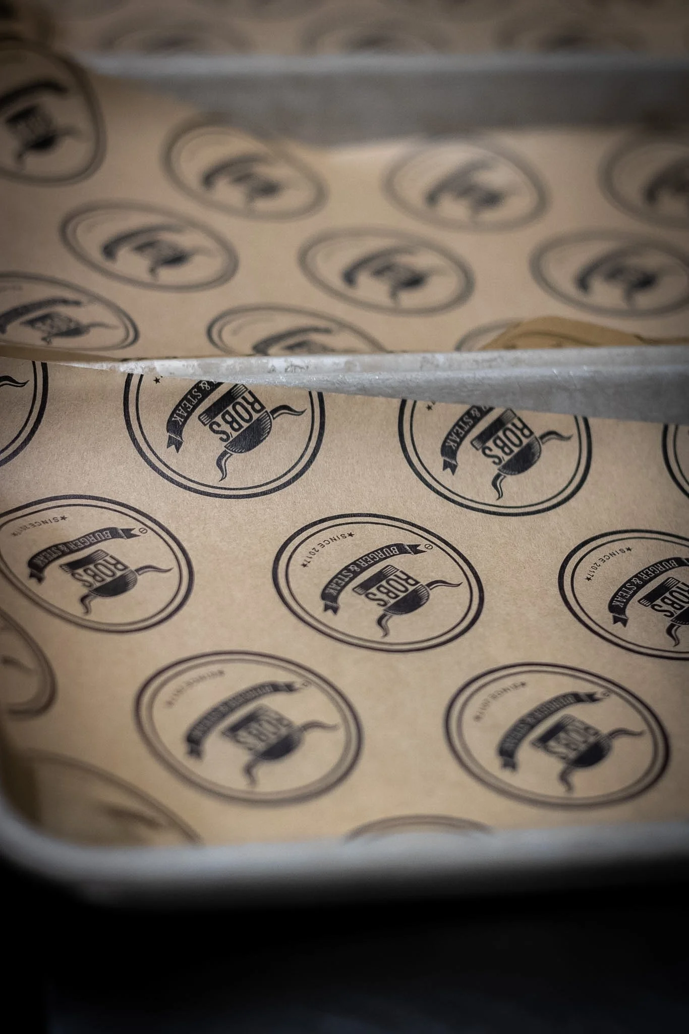 Close-up of beige parchment paper with repeated black logo print that reads 'Rods' and mentions 'Since 2011,' inside a circular border.