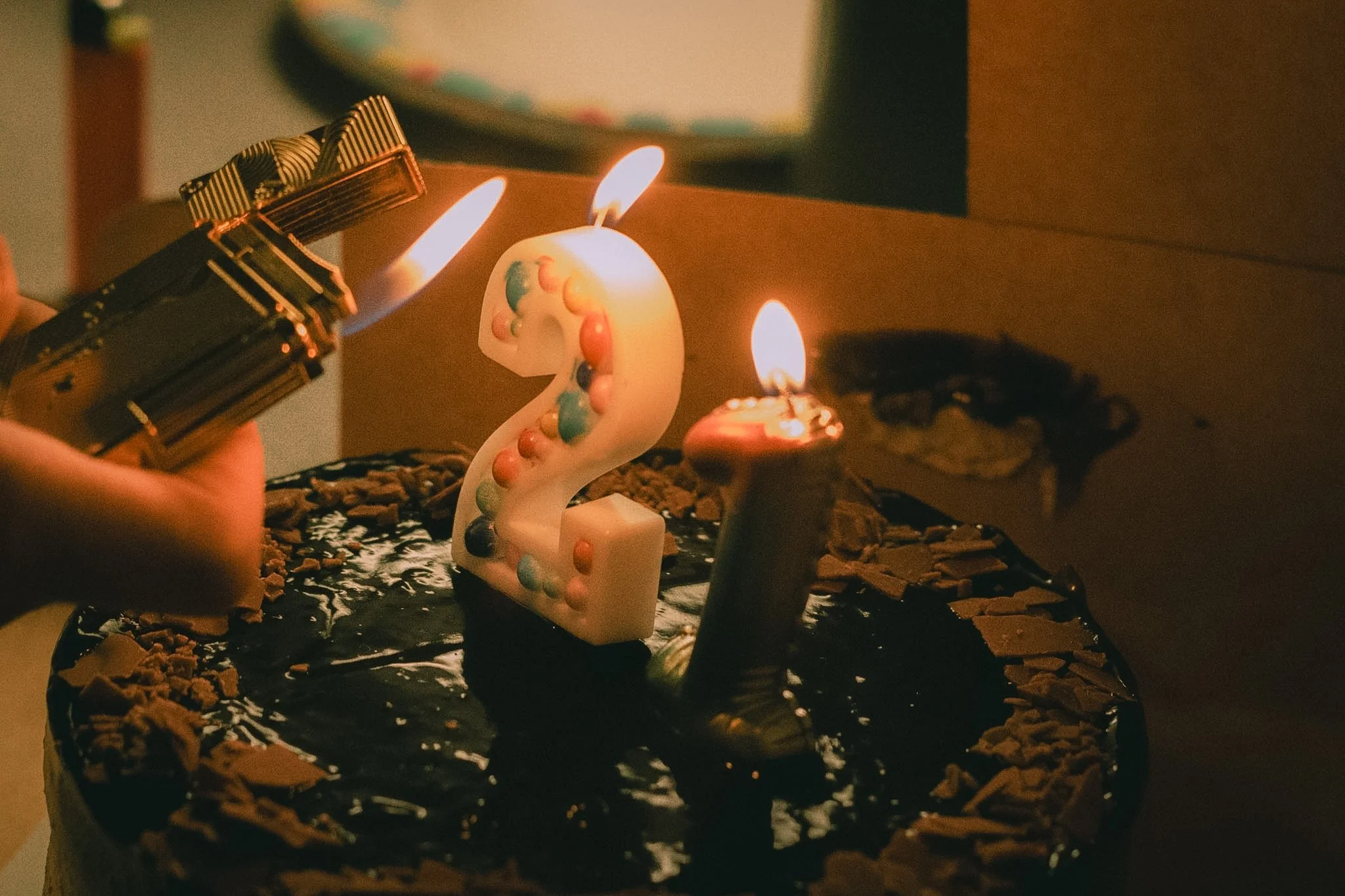 Chocolate birthday cake with colorful candles, a unicorn-shaped candle, and chocolate crumbs, topped with lit birthday candles.