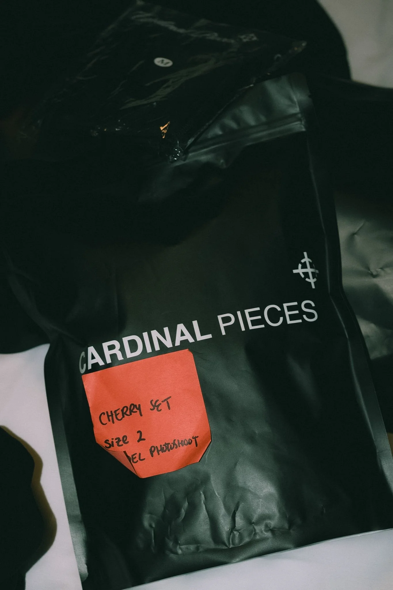 A black bag of Cardinal Pieces Cherry Set size 2, with an orange label attached that says 'Cherry Set size 2' and 'heel photo shoot' written on it.