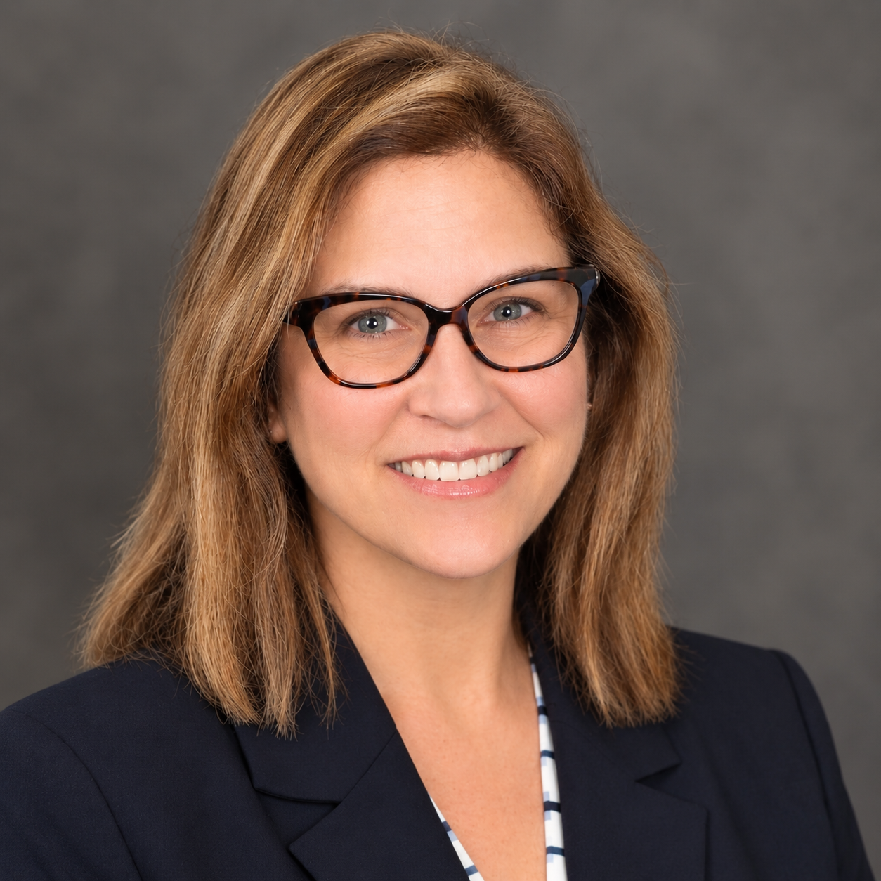 Professional woman with glasses smiling in front of a gray background.
