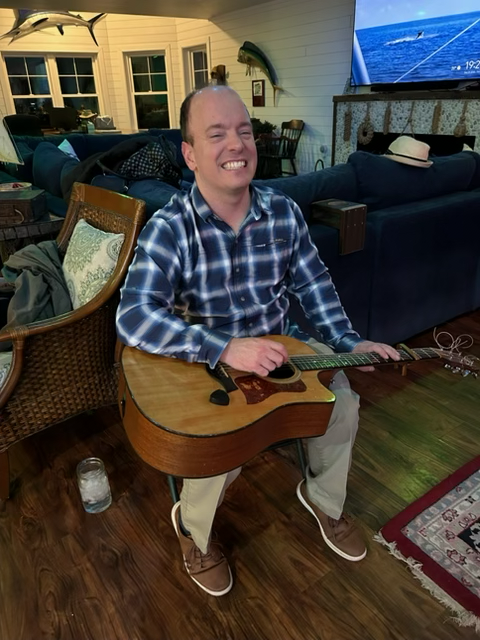 Drake Burd smiling with his guitar in his Buellton living room