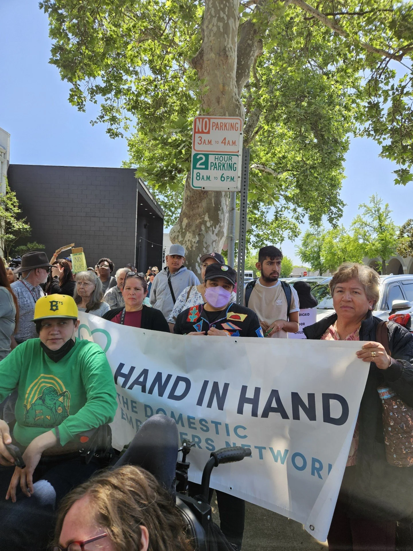 A group of people stand and sit outside with a banner that says Hand in Hand Domestic Employers Network