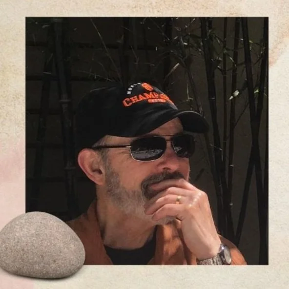 an older man in sunglasses with a beard, holding his chin pensively