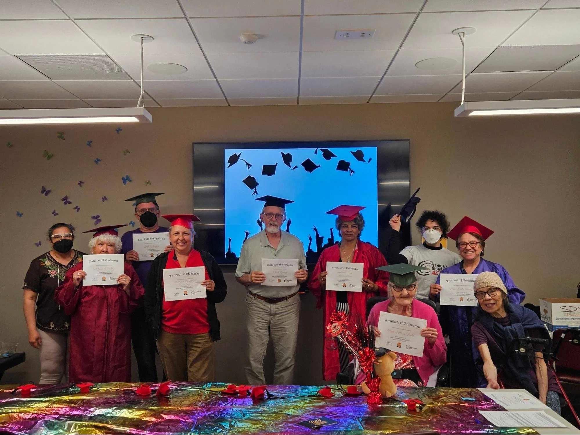 A group of people standing and sitting, many of them in caps and gowns, holding certificates