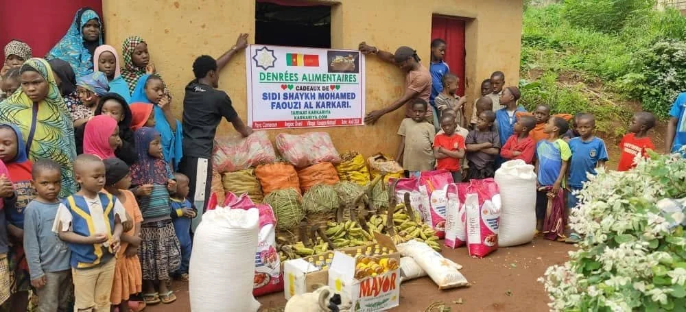 Group of children and adults gathered around food and supplies, with a sign in French and an African flag, indicating a food donation event.