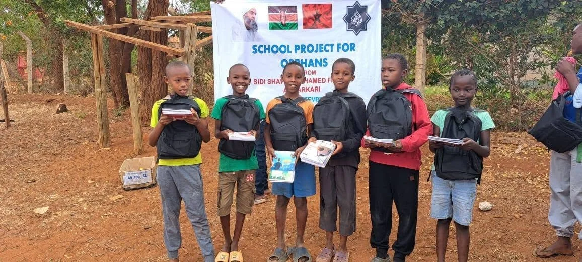 Six children holding notebooks and backpacks in front of a banner for a school project for orphans in Kenya.