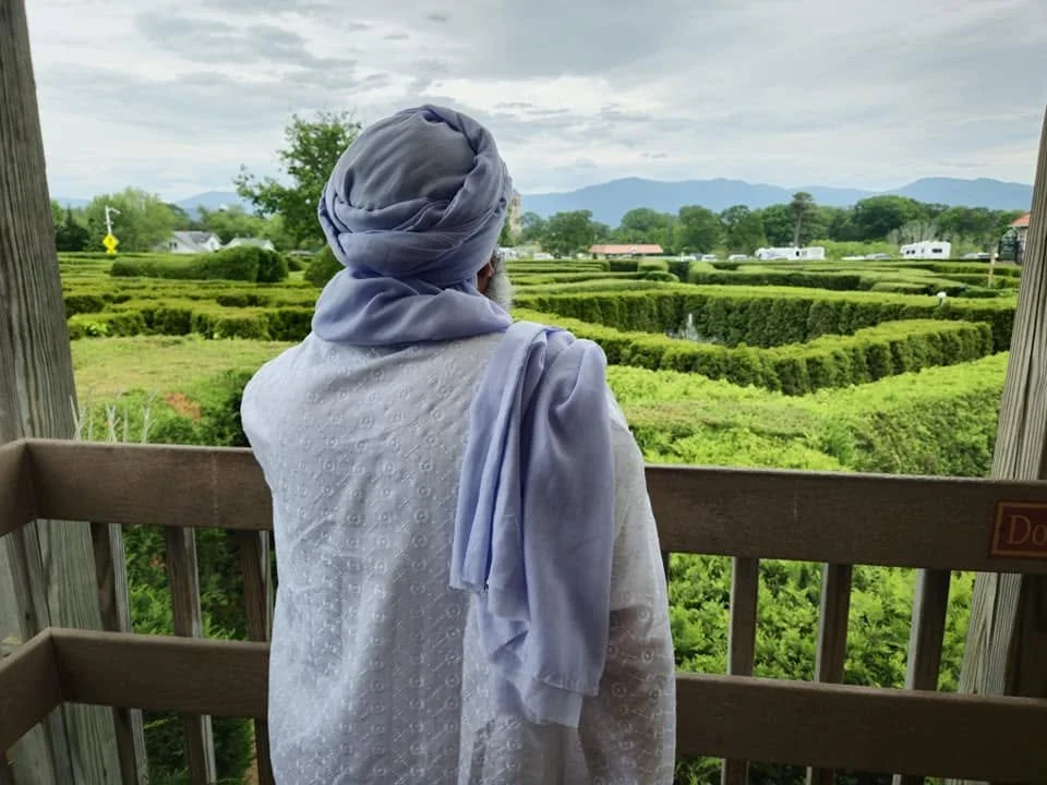 Person wearing a headscarf looking at a lush green hedge maze from a wooden observation deck.