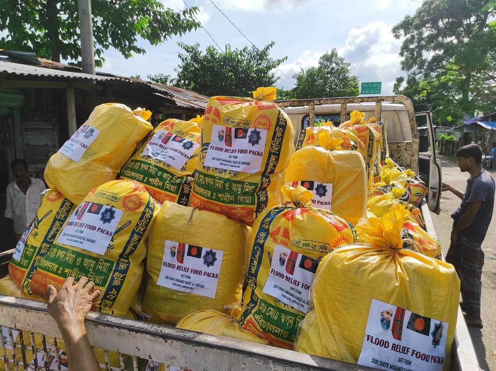Yellow bags labeled as flood relief food packs on a truck, with people in the background.