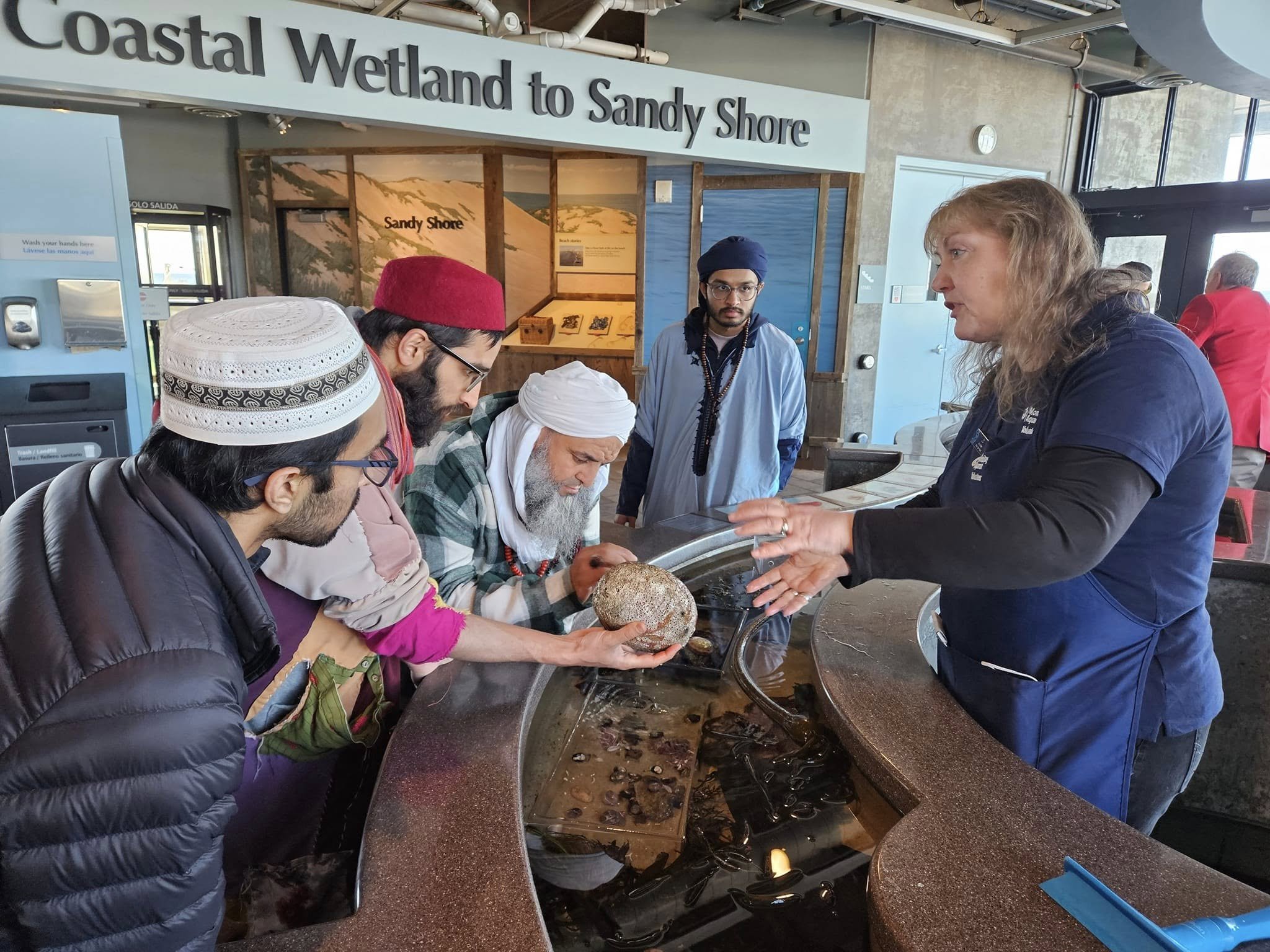 People at a counter ordering food or beverages inside a cafe or restaurant with a sign that reads 'Coastal Wetland to Sandy Shore' in the background.