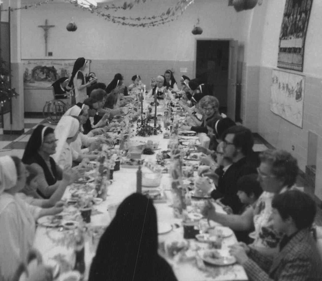 Black and white photo of a large group of nuns and people seated at a long dinner table decorated with a menorah, celebrating a religious or festive occasion.