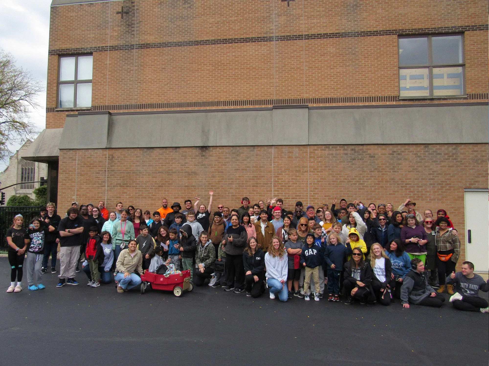 Group photo of dozens of people, from kids to adults, in front of a brick building.