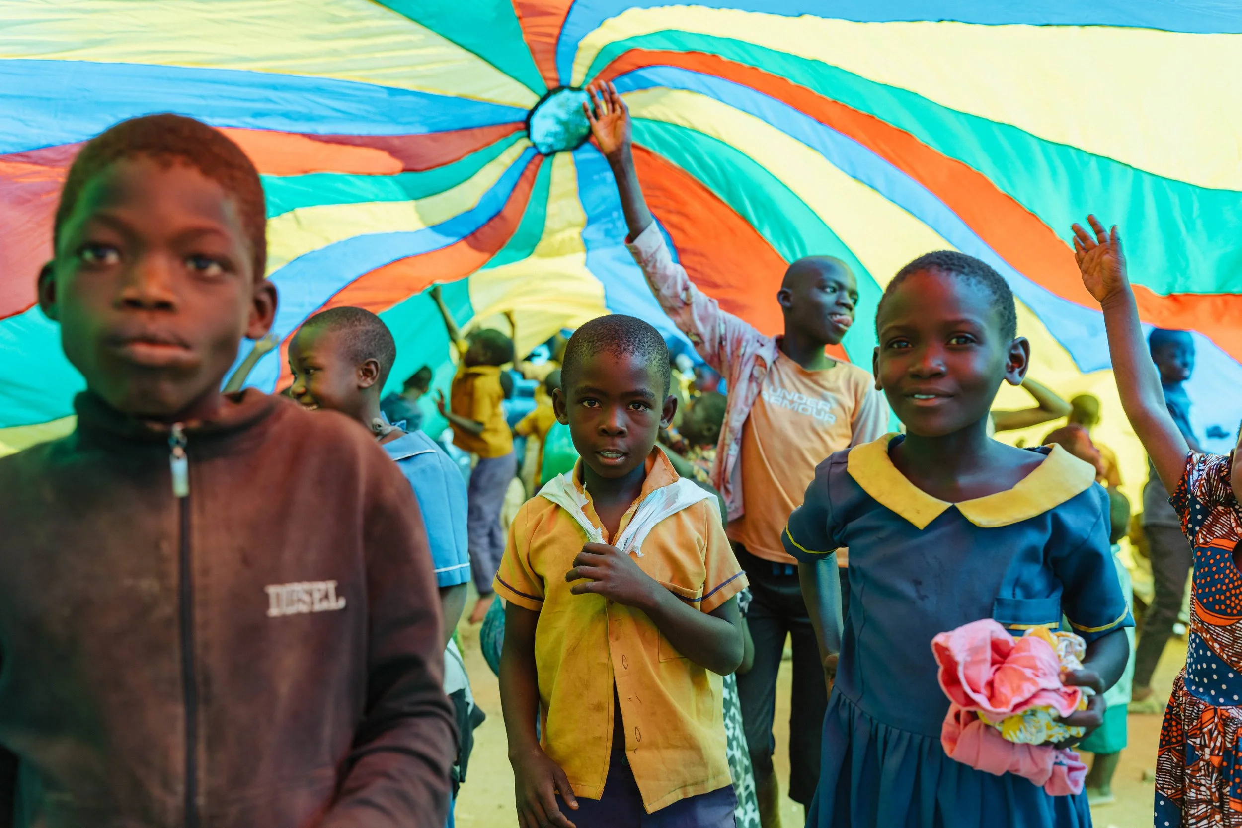 Children holding a colorful parachute during outdoor activity.