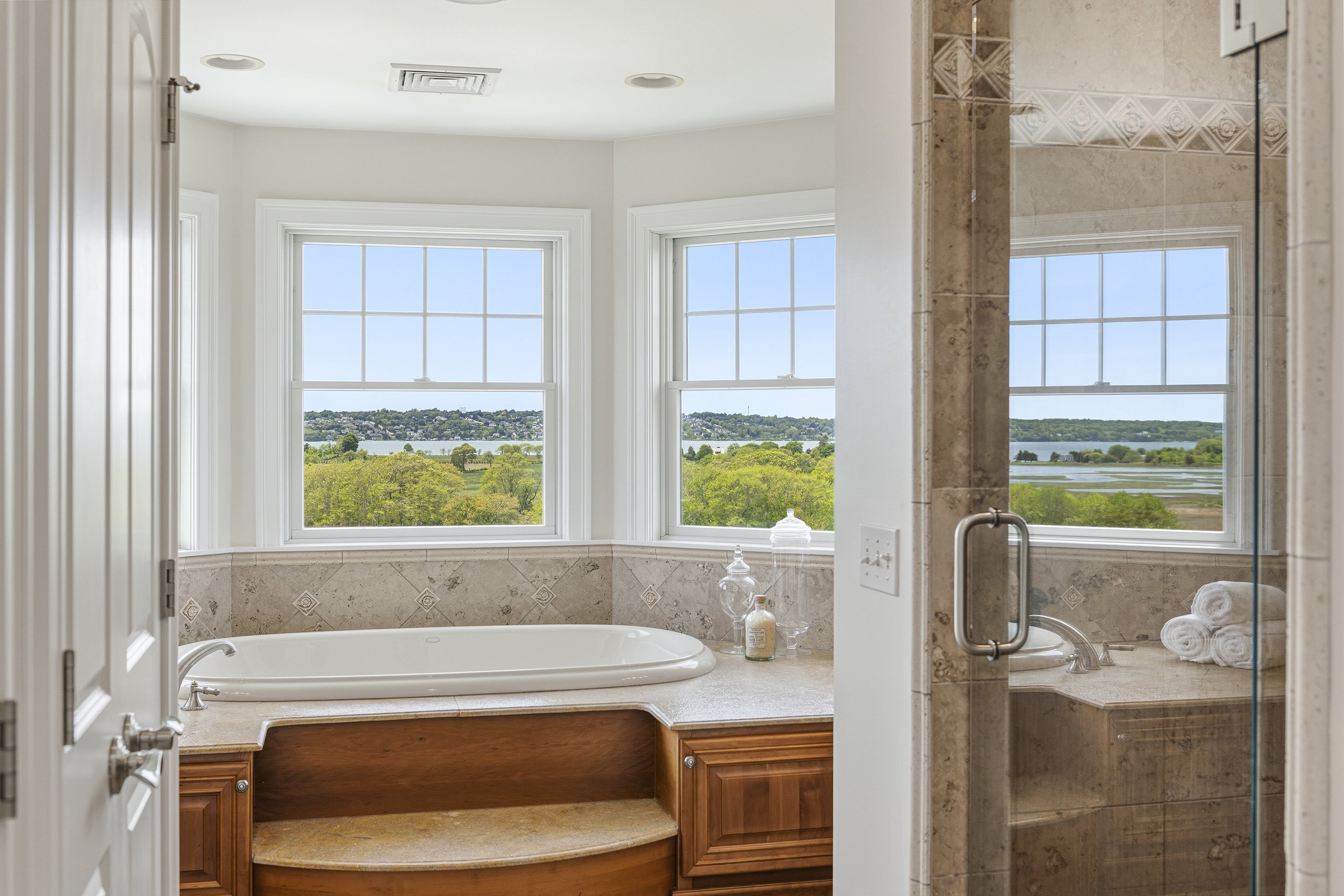 Bathroom with large windows overlooking a river and trees, bathtub, and marble accents.