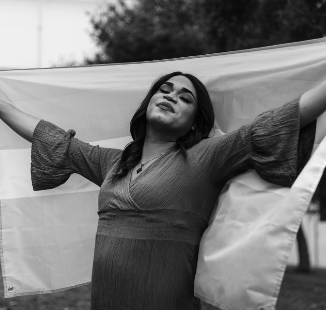 person standing with trans or transgender pride flag experiencing joy and stress from gender transition