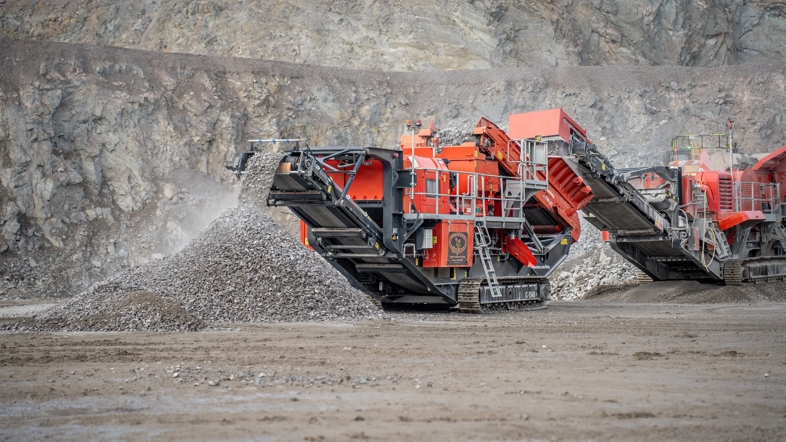 A large red industrial rock crusher machine in a quarry, crushing rocks and gravel into smaller pieces.