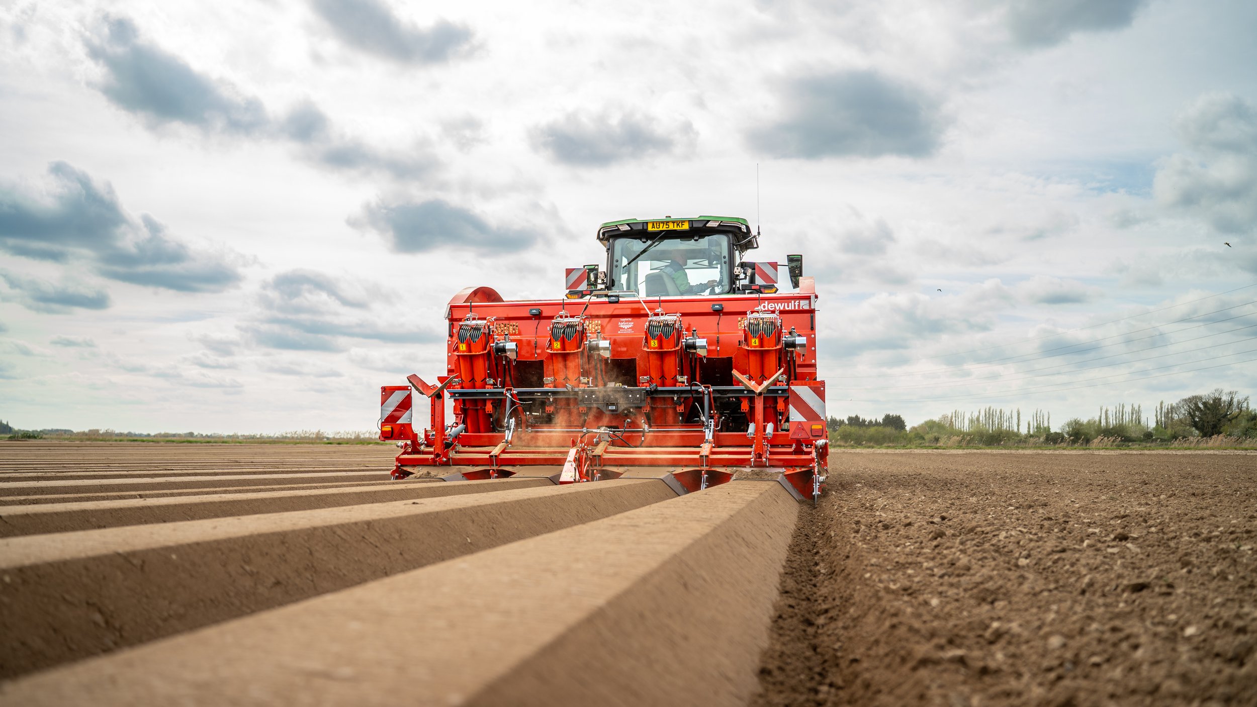 A red tractor tilling a field under a cloudy sky.