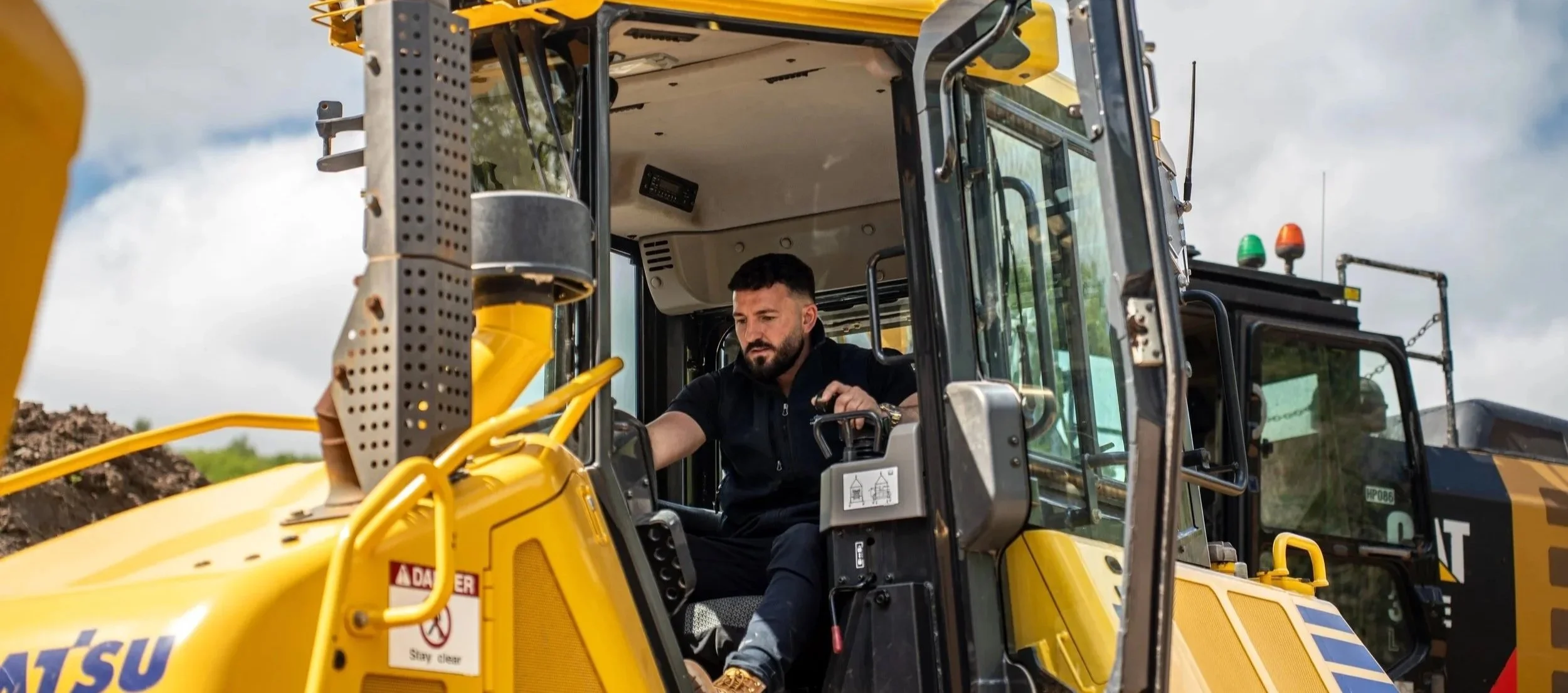 A man operating a yellow Caterpillar backhoe loader outdoors during daytime.