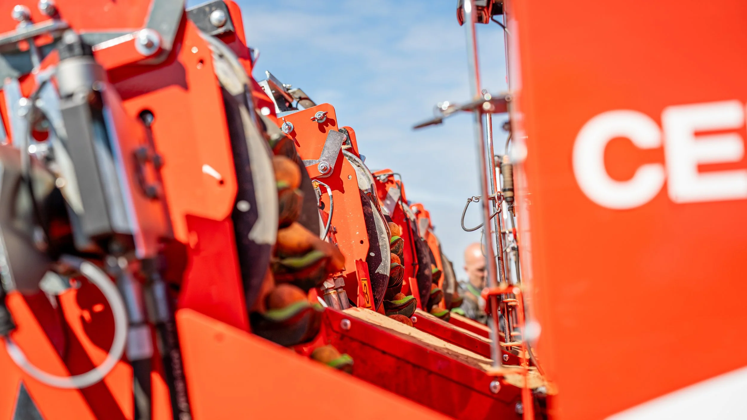 Close-up of multiple orange firefighting tools and equipment on a fire truck, with a man in a reflective uniform visible in the background.