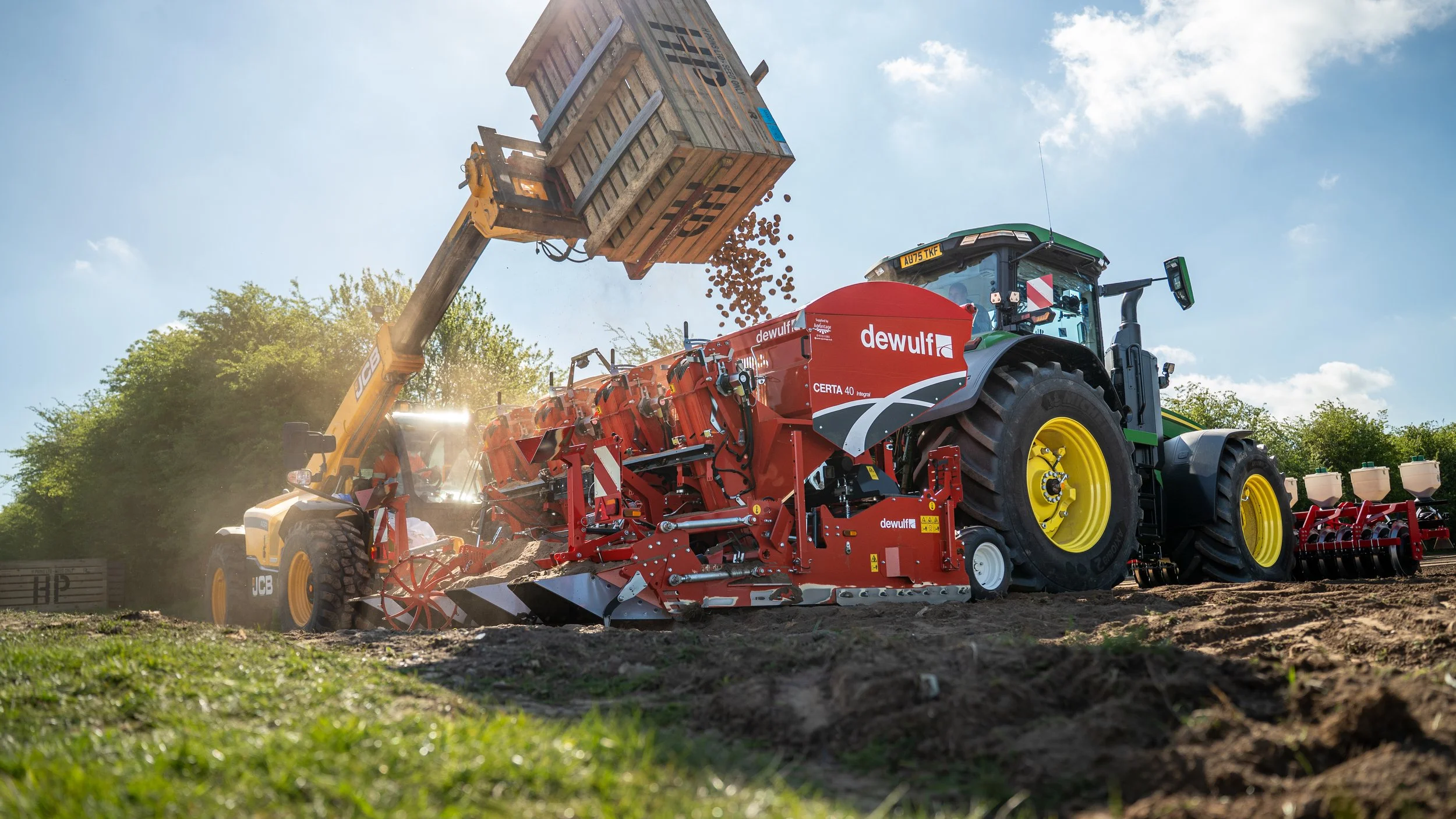 A tractor pulling a red soil preparation machine with multiple rotating blades, working on a farm field.
