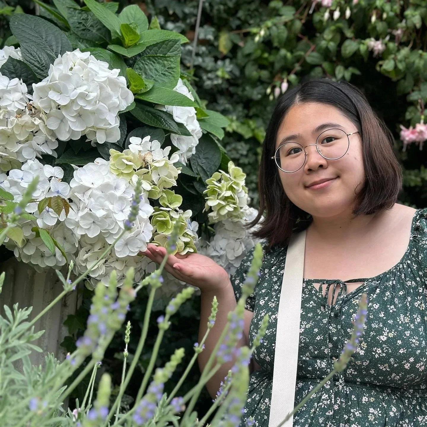 Image of a woman with glasses smiling and touching white hydrangea flowers in a garden.