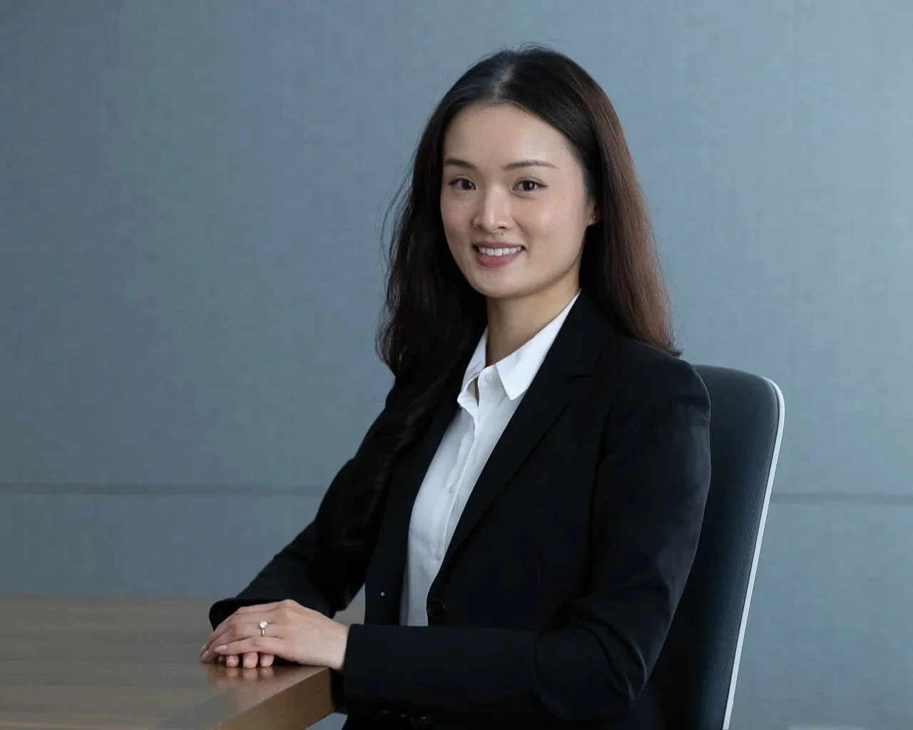 A young woman in a black blazer and white shirt sitting at a desk in an office setting.