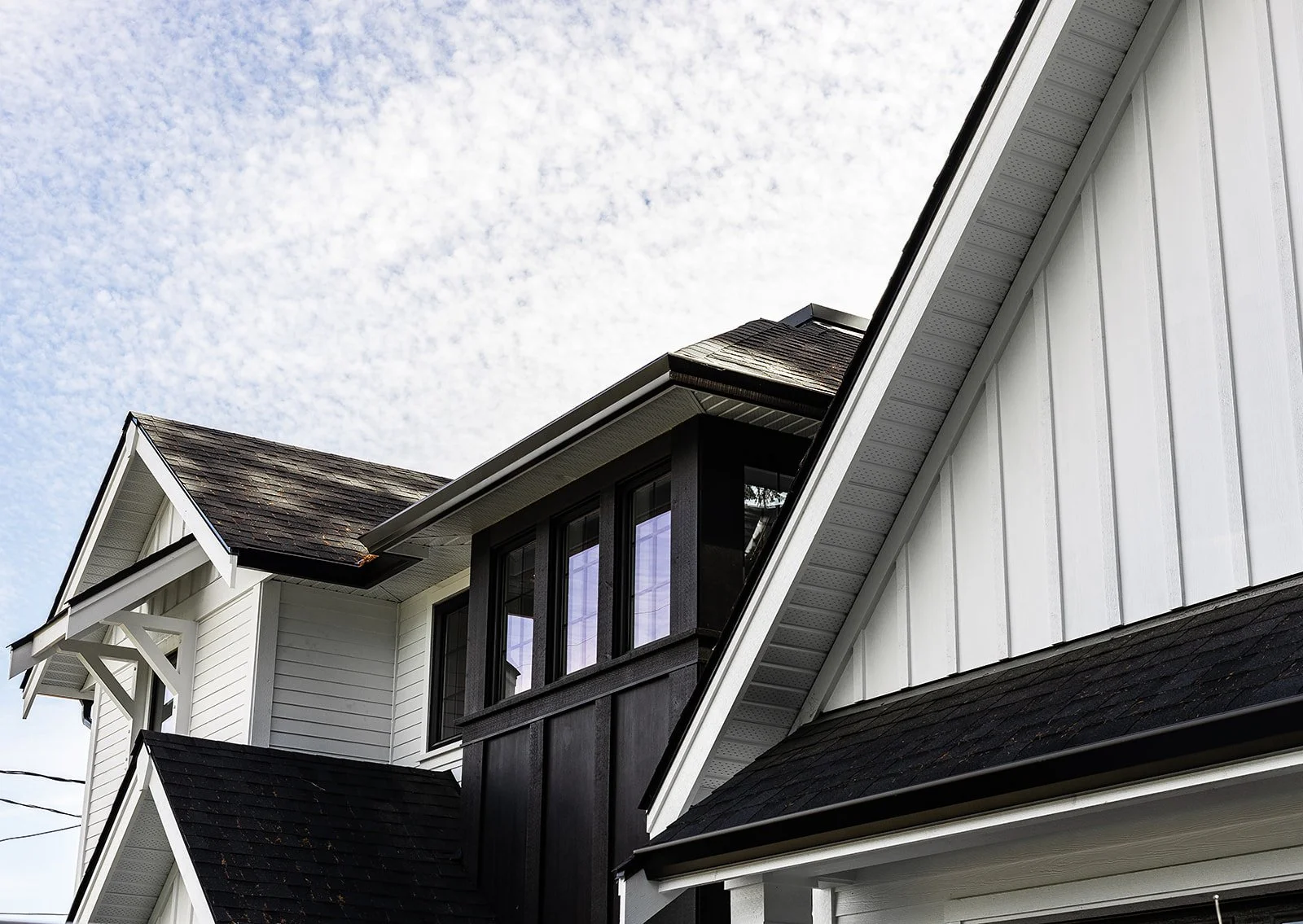 Close-up view of the rooftops of modern houses with black and white exterior siding and dark shingles, under a cloudy sky.