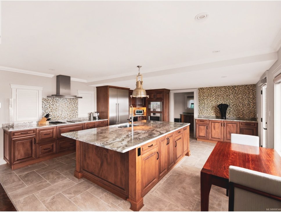 Modern kitchen with wooden cabinets, a granite island, stainless steel appliances, and a dining table with chairs.