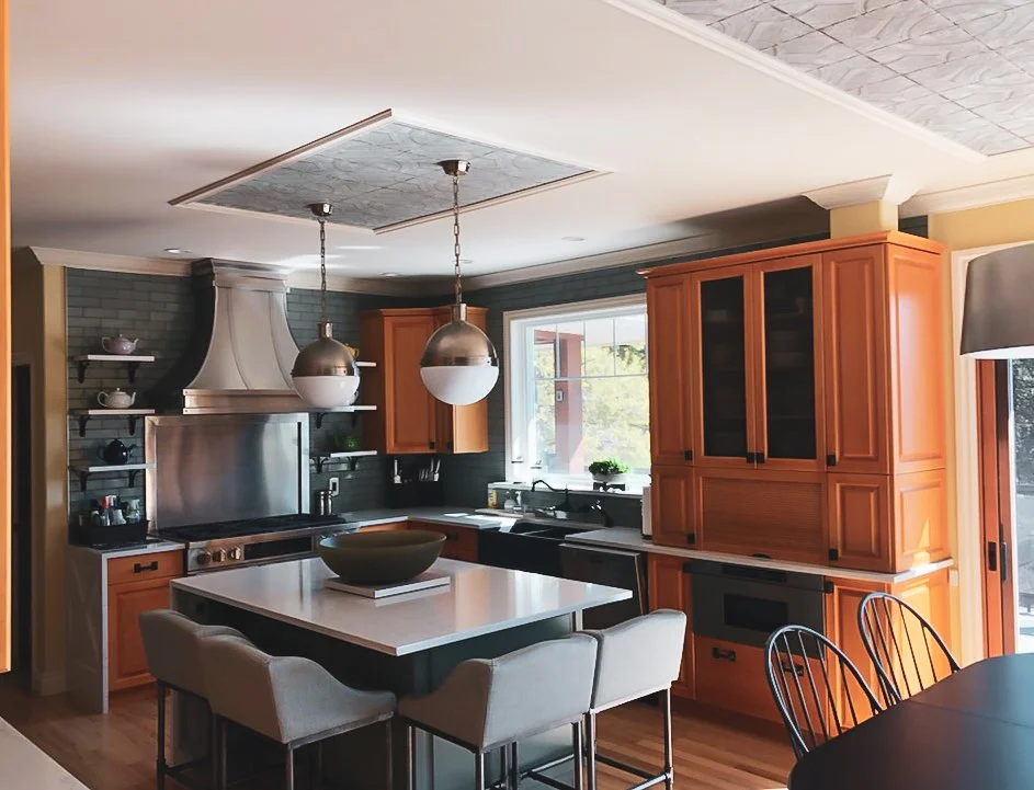 Modern kitchen with wooden cabinets, stainless steel range hood, island with seating, pendant lighting, window, and open shelves.