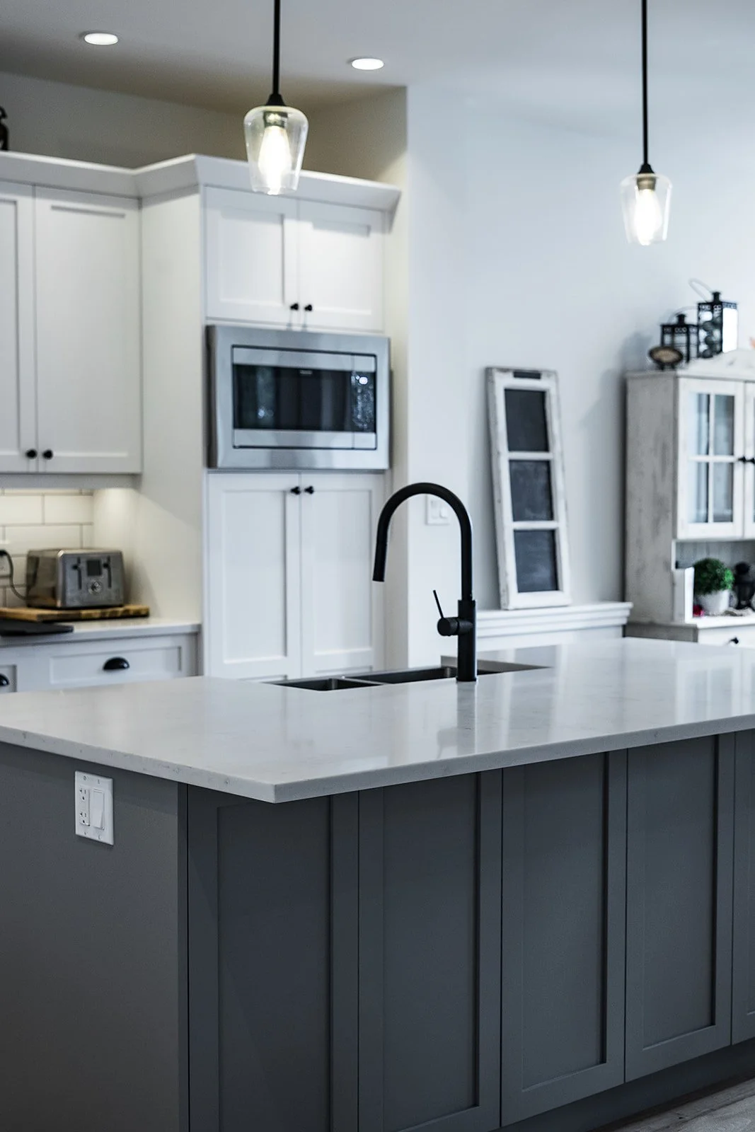 Modern kitchen with white cabinets, black faucet, gray island, built-in microwave oven, stainless steel toaster, and decorative items.