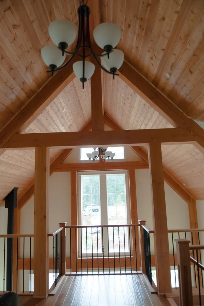 Interior view of a room with a high, vaulted wooden ceiling, chandelier, large window, and wooden railings.