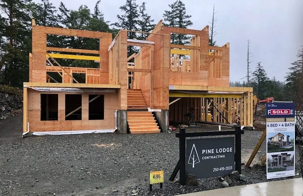 A wooden house under construction in a wooded area with a sign for Pine Lodge Contracting and a sold sign showing 4 bedrooms and 4 bathrooms.