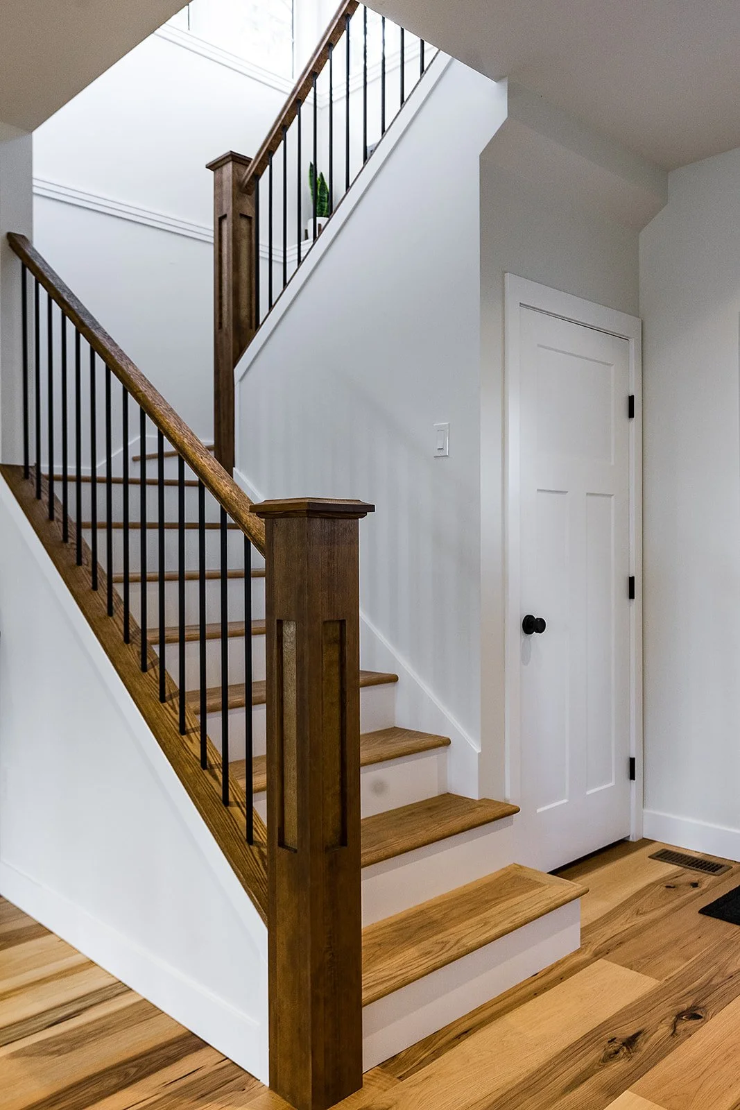 Interior view of a staircase with wooden steps, black metal balusters, and white walls, next to a white door.