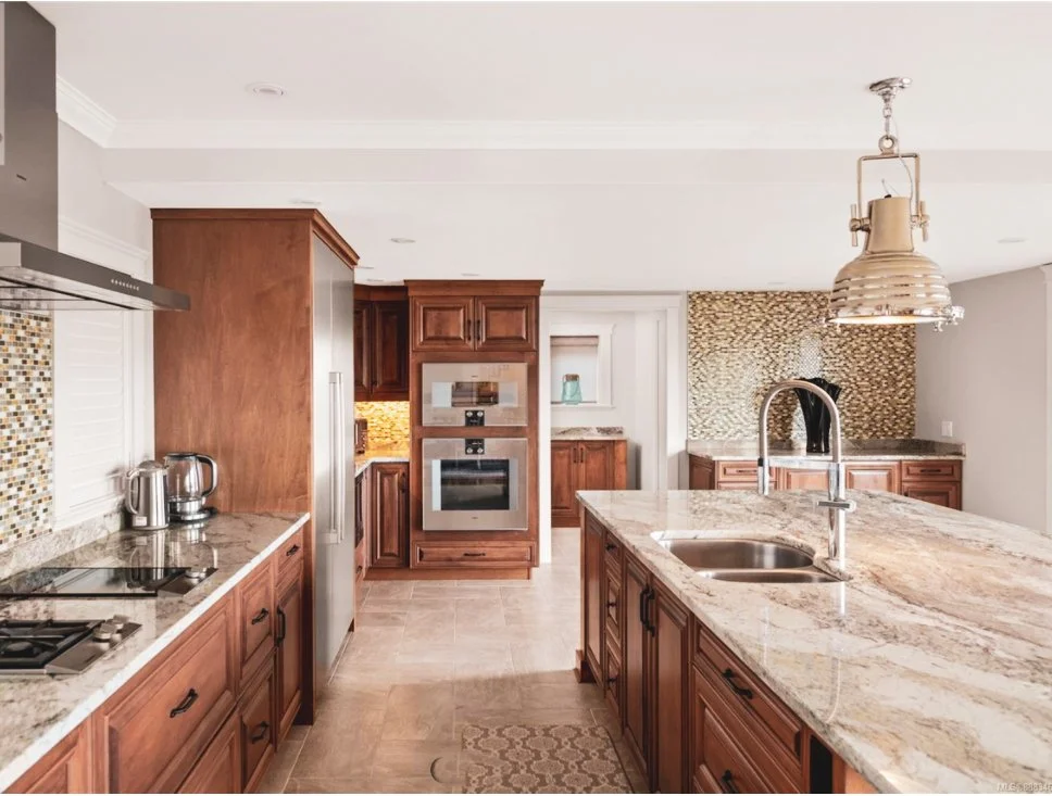 Modern kitchen with wooden cabinets, granite countertop island, stainless steel appliances, and a mosaic tile backsplash.