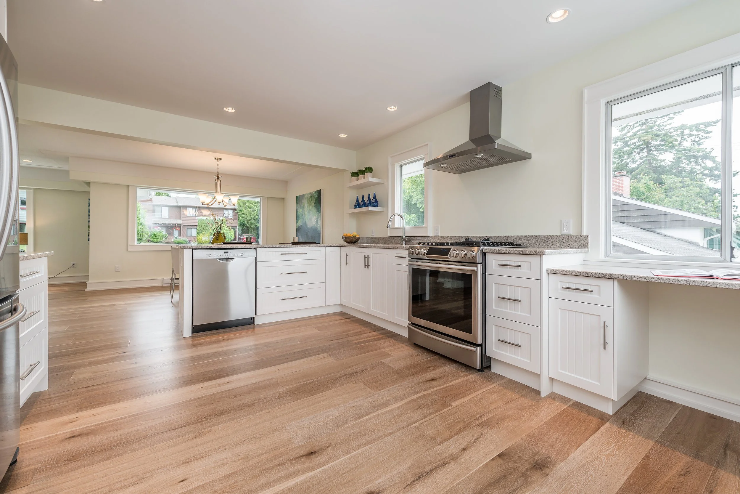 Bright and modern kitchen with white cabinets, stainless steel appliances, a large window, and wood flooring.