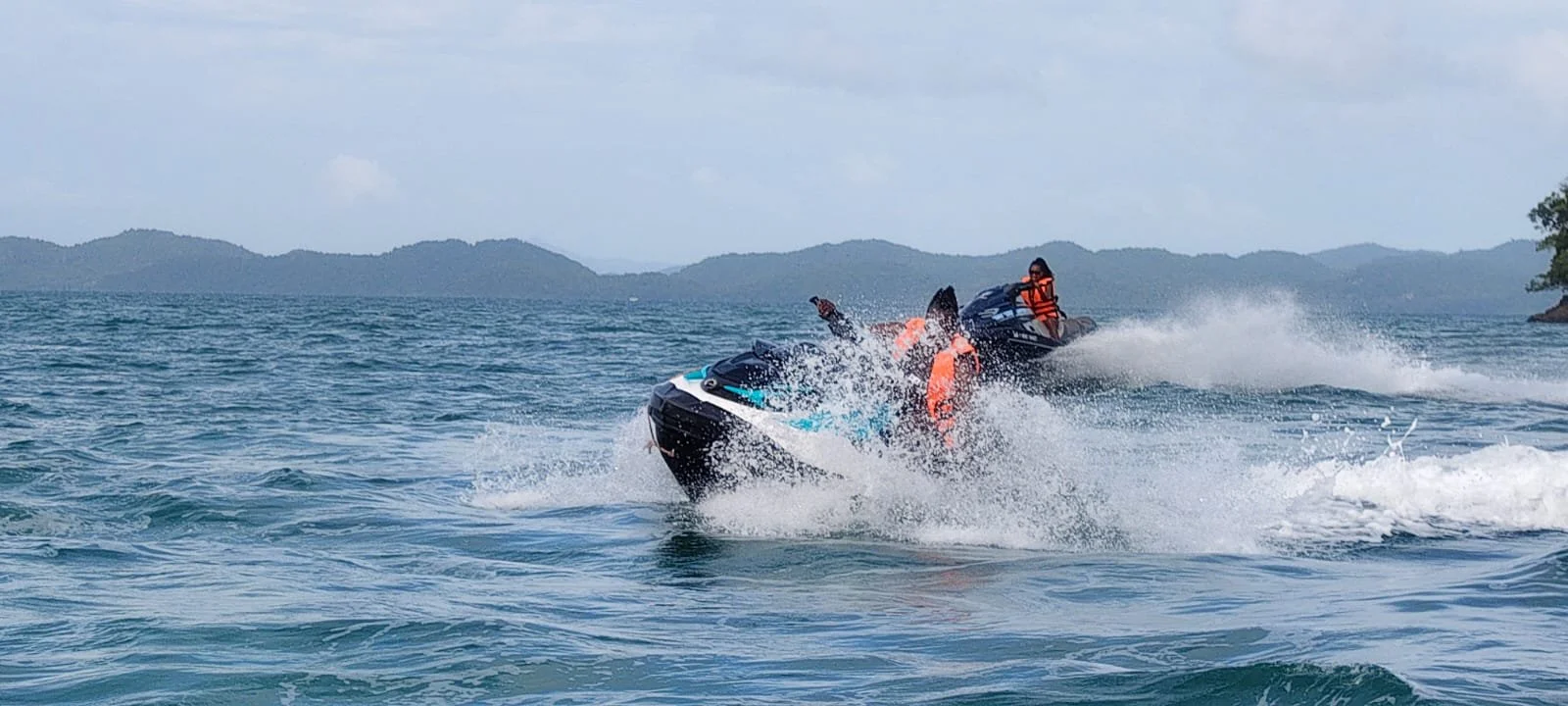 People riding jet skis on the water with a mountain landscape in the background.