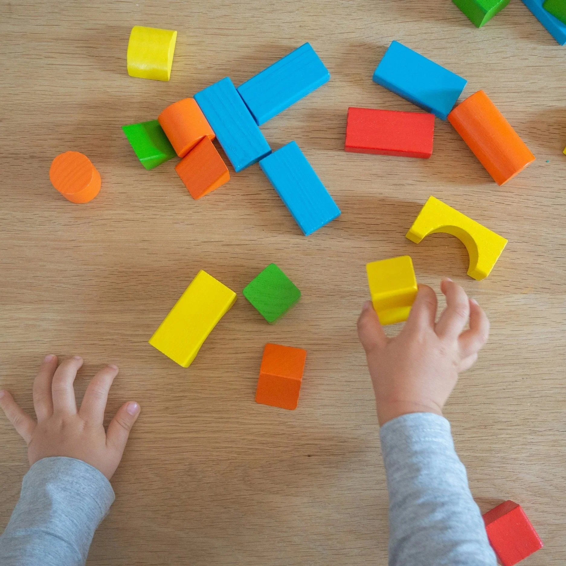 Children playing with colorful wooden blocks on a wooden surface.