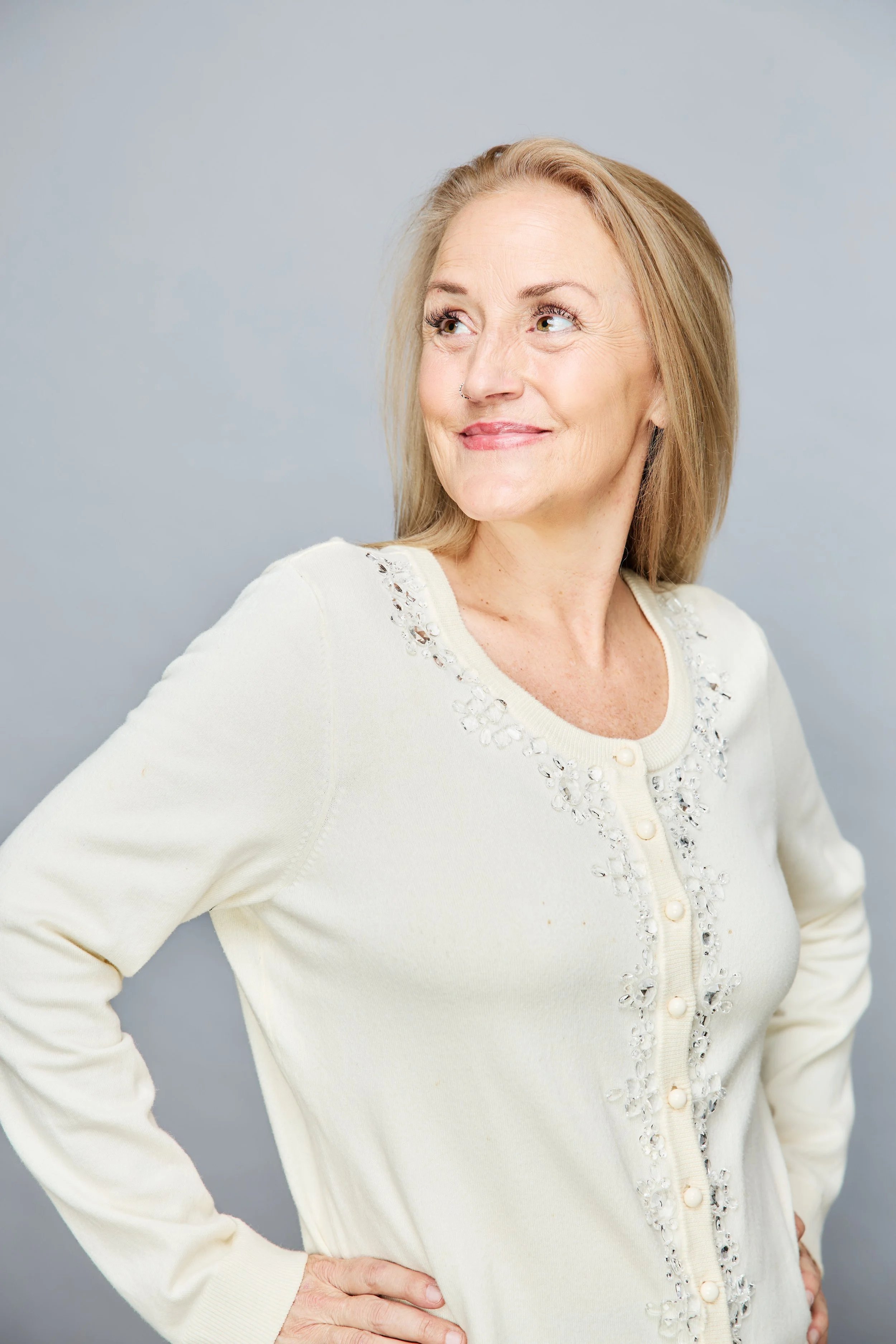 Woman smiling in cream sweater with embroidered details against a light background
