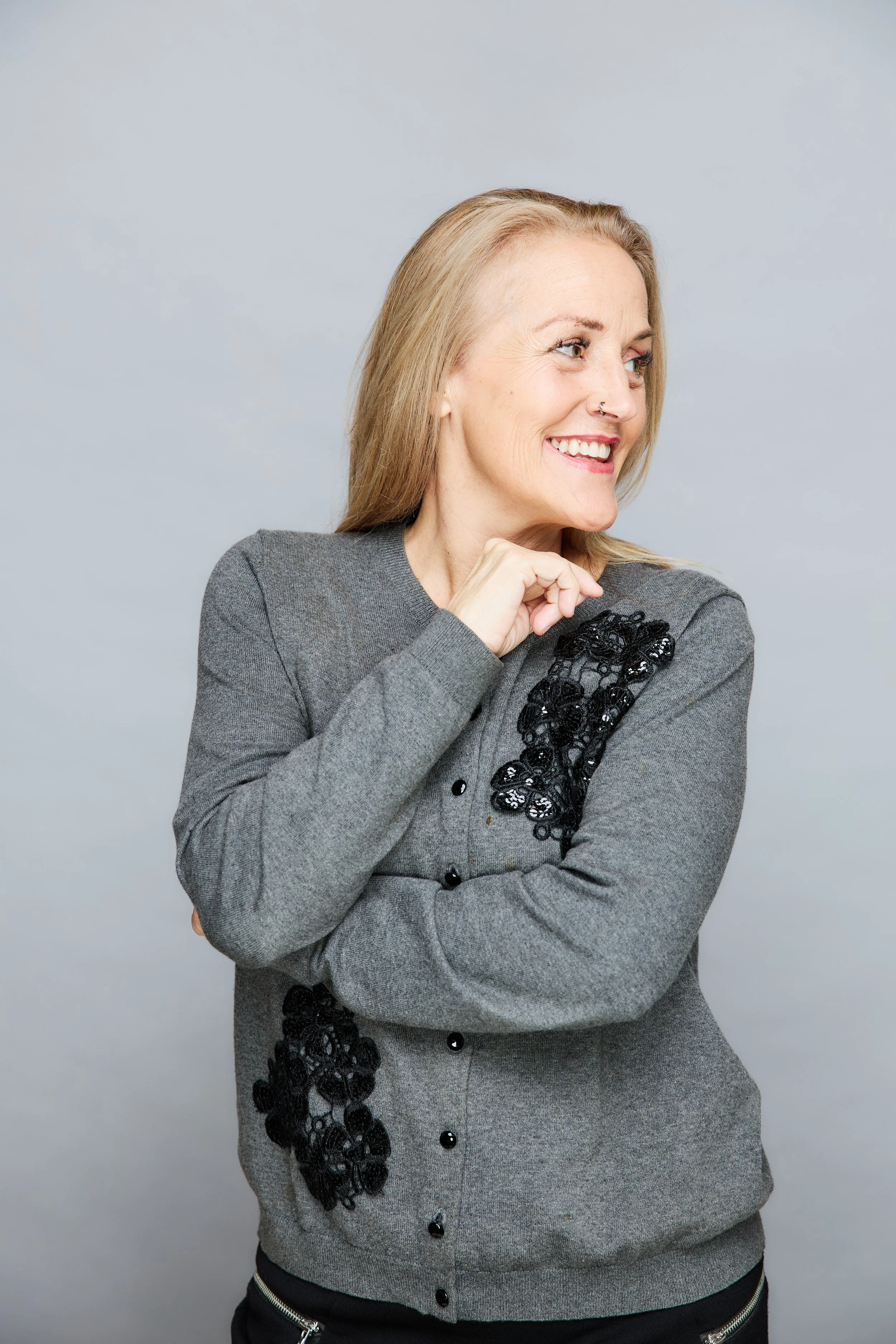 Smiling blonde woman in gray sweater looking to the side against a soft gray background
