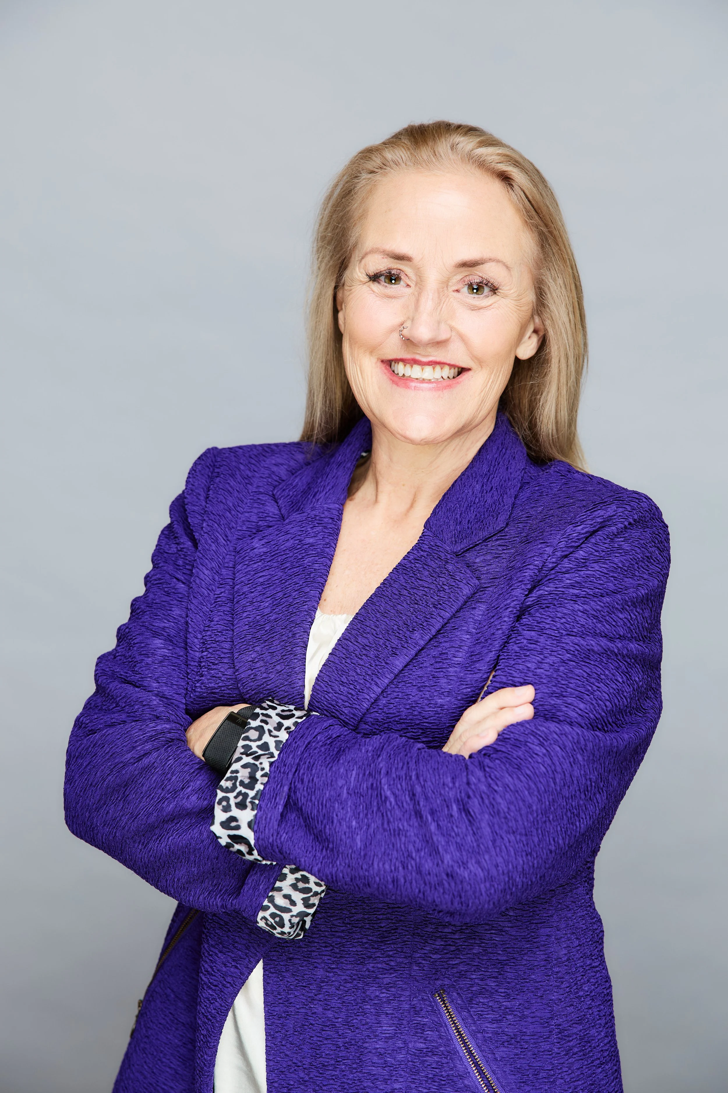 Smiling woman in textured purple blazer with arms crossed against a neutral background