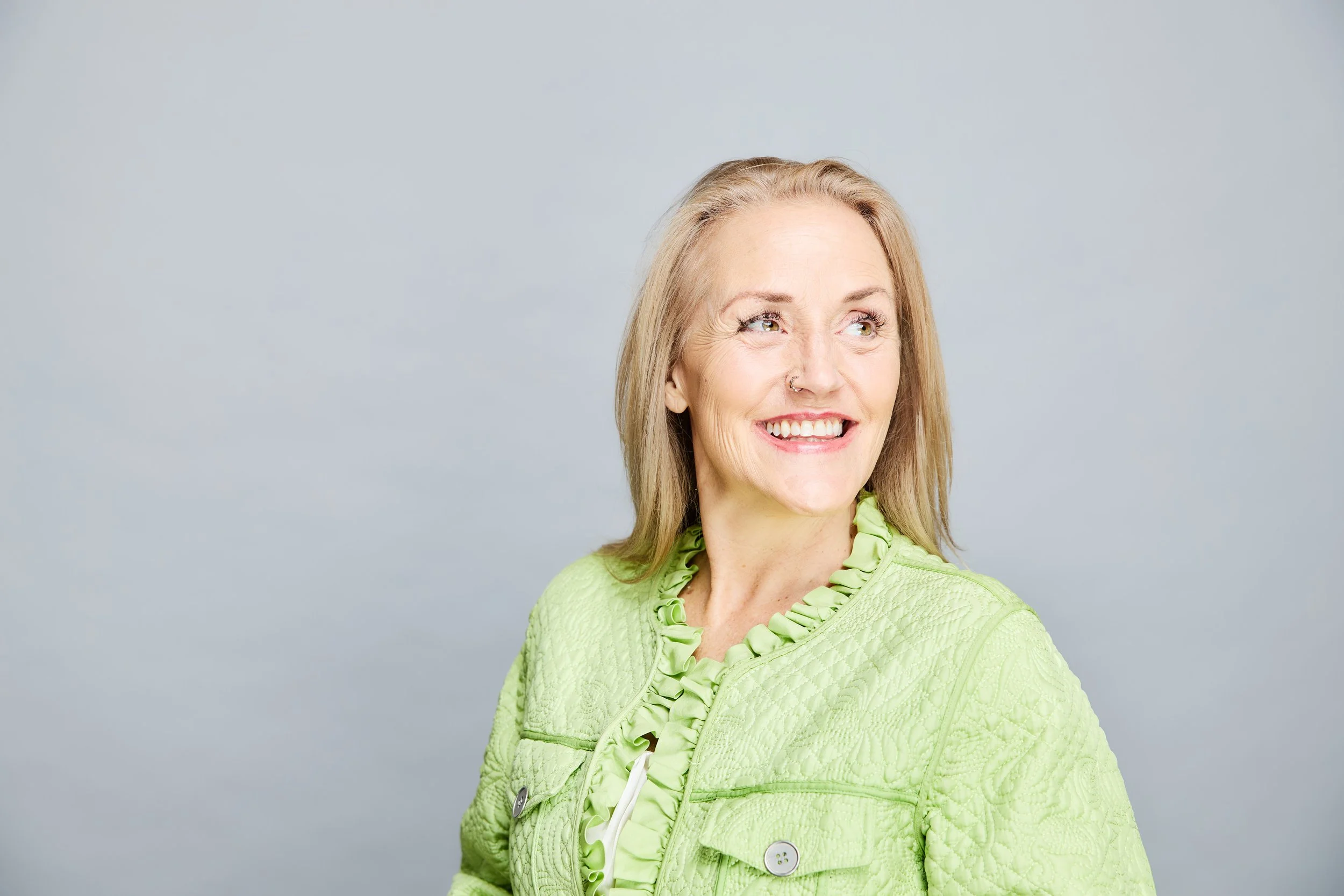 Smiling blonde woman in textured green jacket against a soft gray background