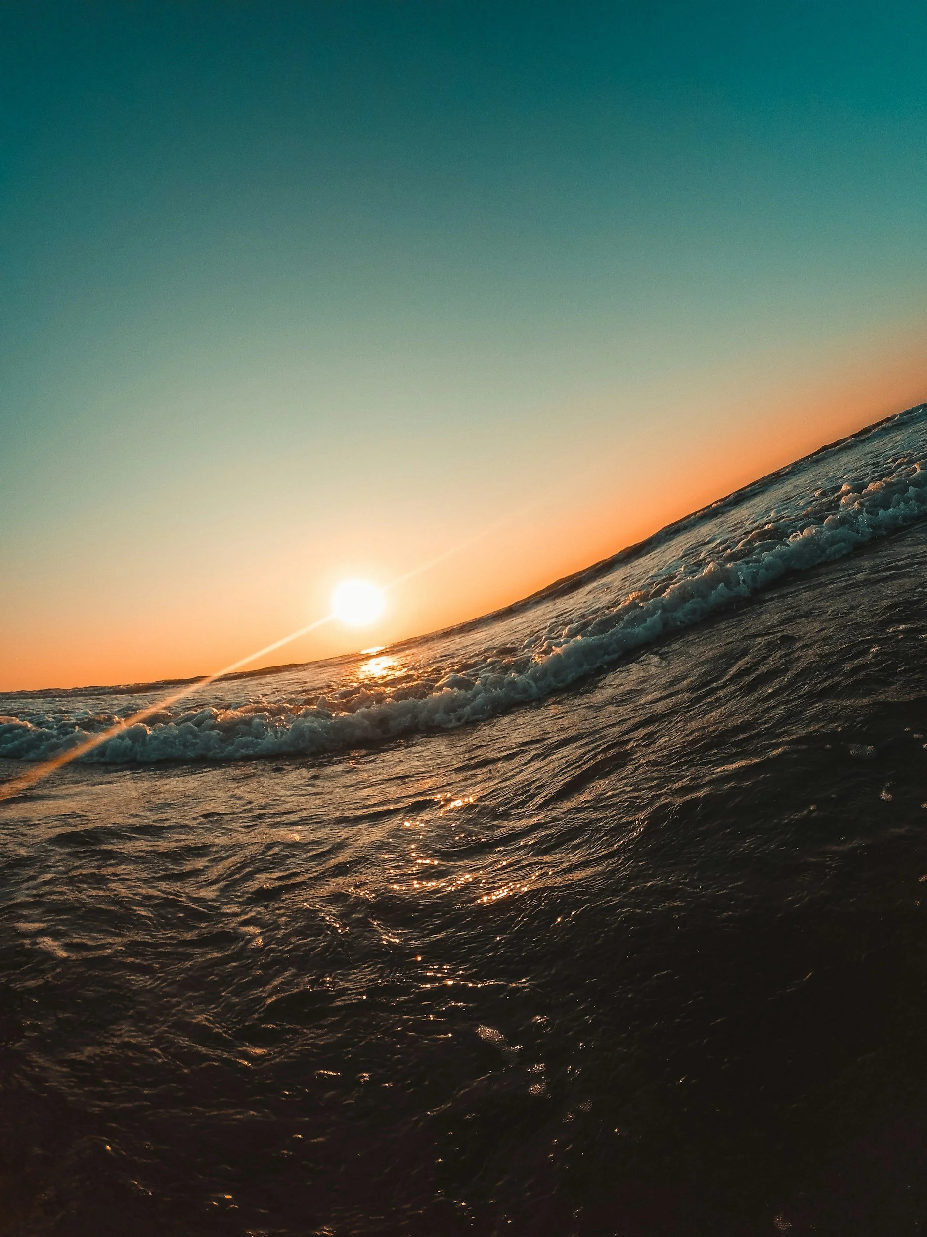 Sunset over ocean with waves and colorful sky that dances with the the horizon curved like the world smiles back.