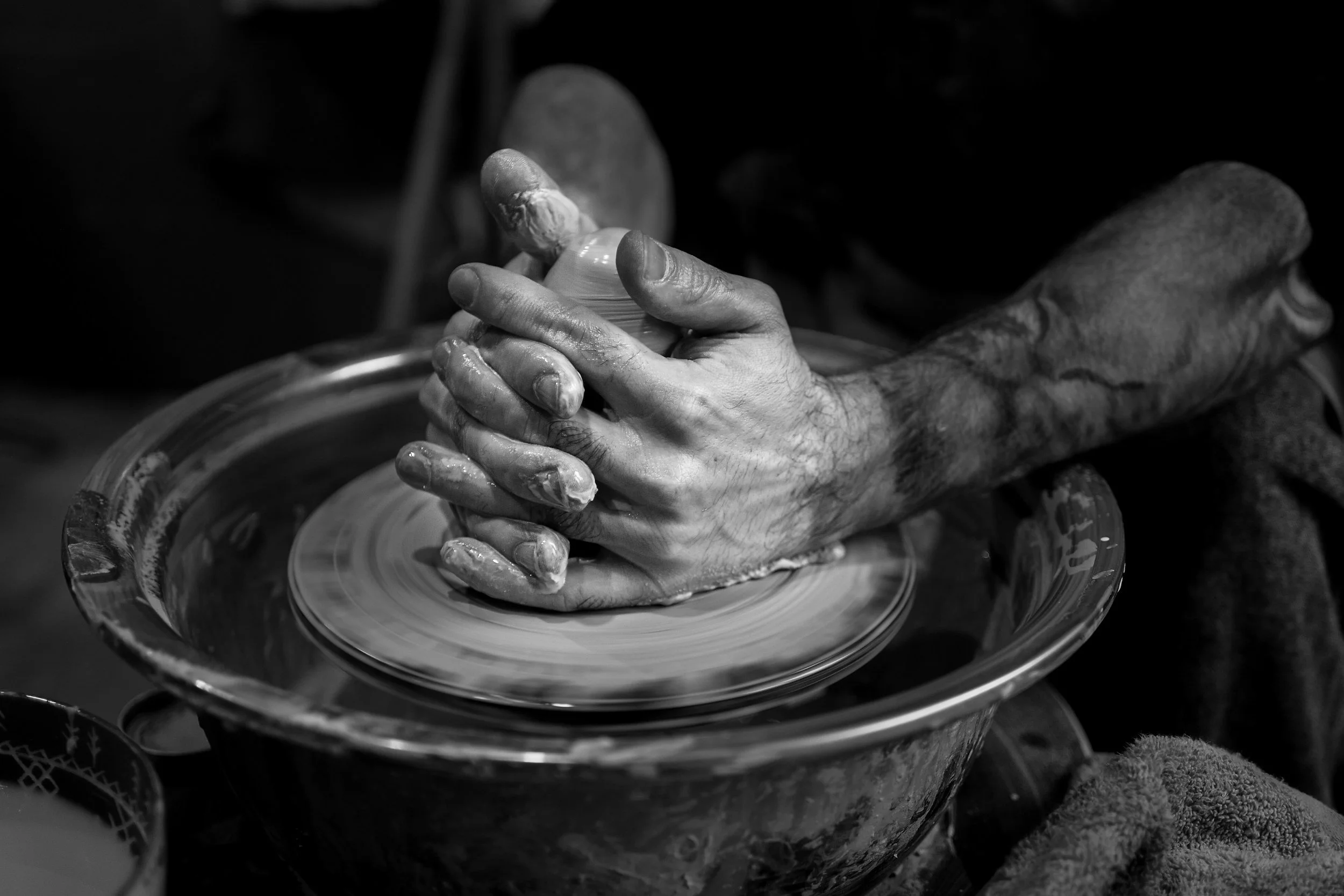 Close-up of a person's hands shaping clay on a pottery wheel in black and white. Forging our future we decide the shape, texture & colors we move forward with.