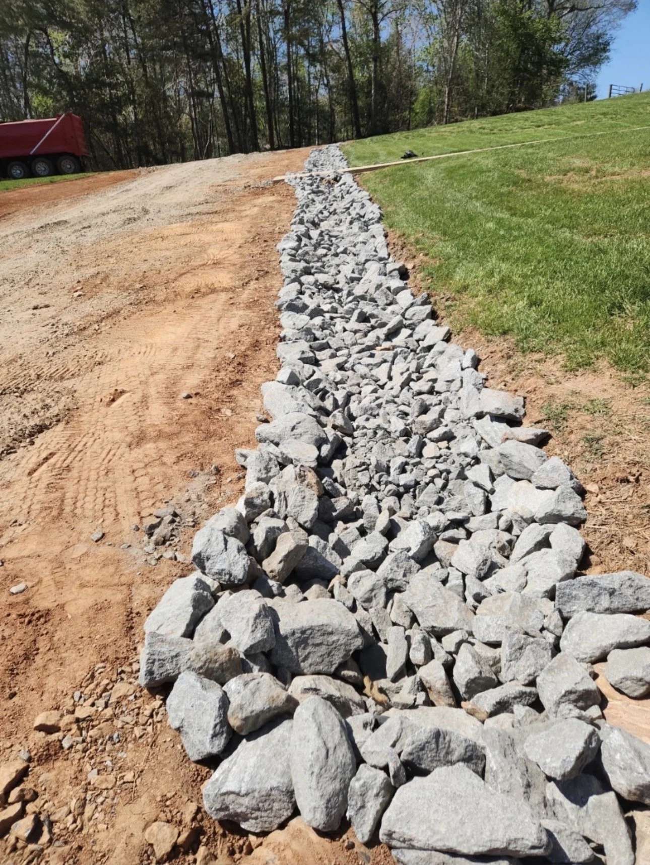 A line of rocks placed along a dirt path on one side and grass on the other, with construction equipment in the background.