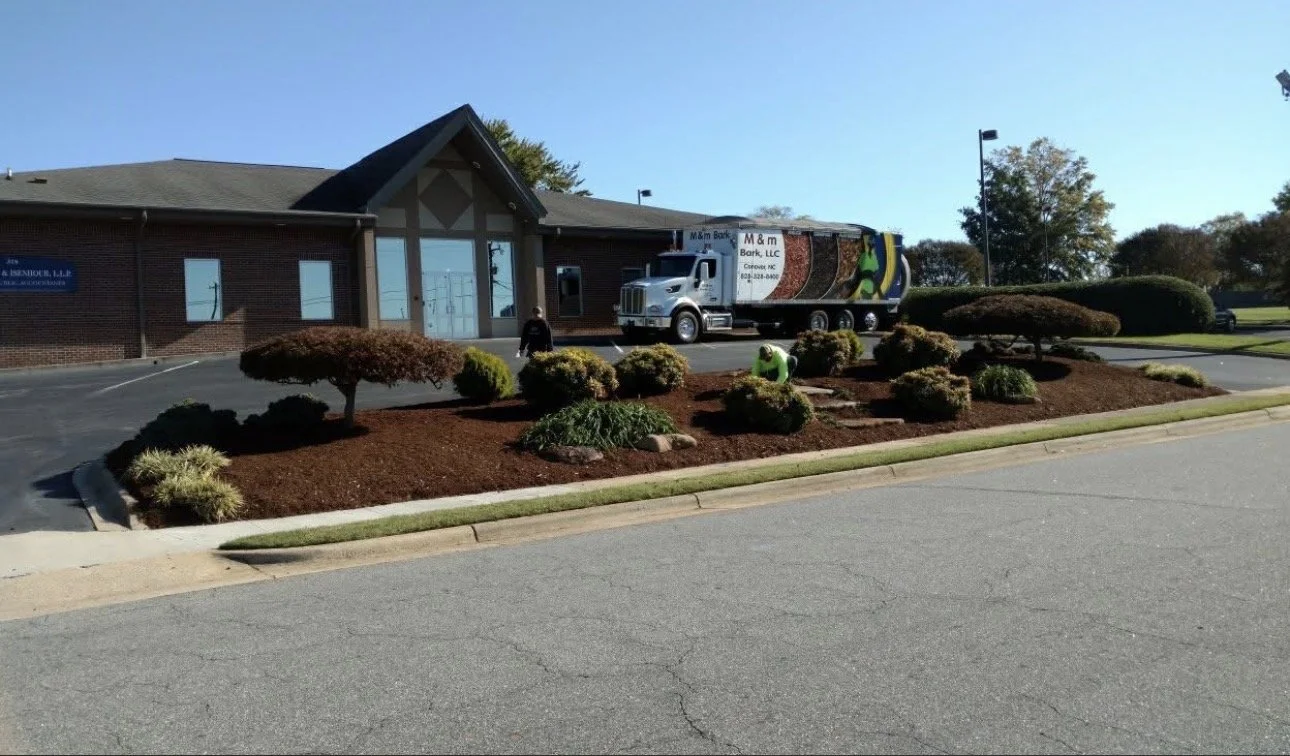 A building with landscaped bushes and mulch, a sidewalk, a person walking, and a truck parked in front of the building on a clear day.