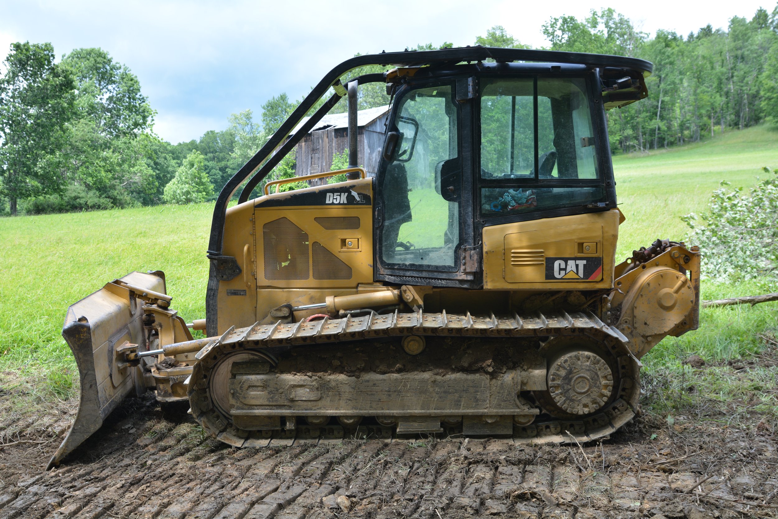 CAT D5k Dozer Sitting on a road it just built in Punxsutawney on a Sunny Summer Day with a field and trees in the background along with sky and clouds