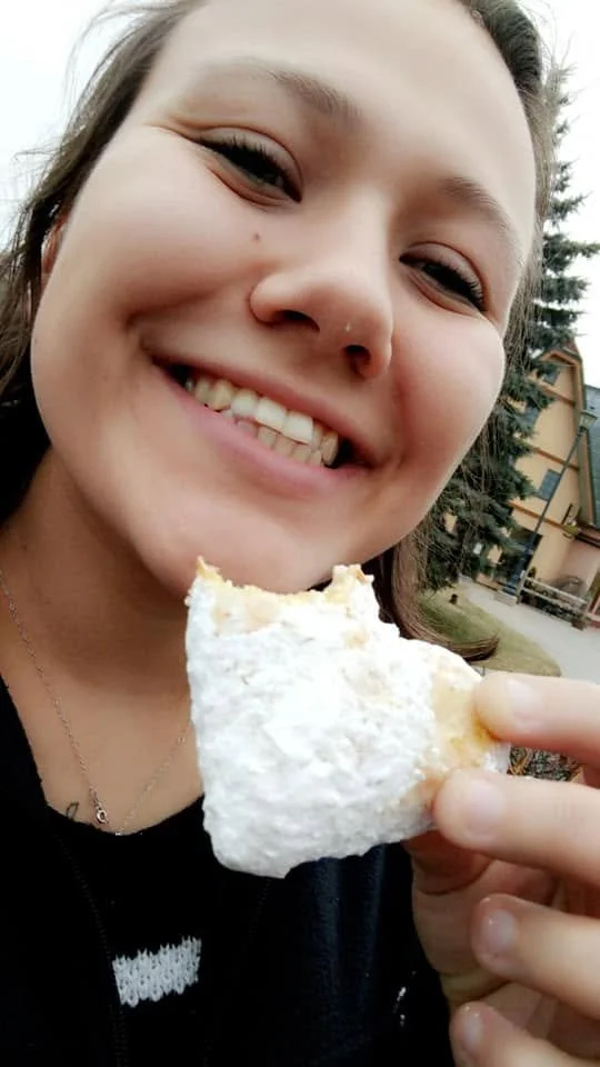 Young woman smiling and holding a piece of ice cream cone outdoors.